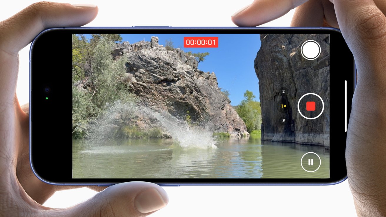 Hands holding a smartphone recording a video of a splash in a river with rocky cliffs and trees in the background.