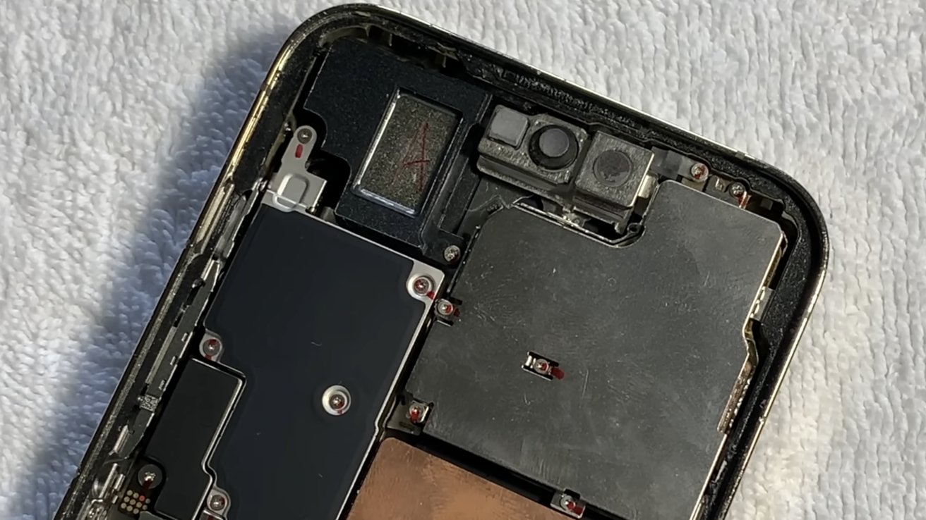 Close-up of a smartphone's internal components, showing connectors, screws, and metal casings on a white textured surface.