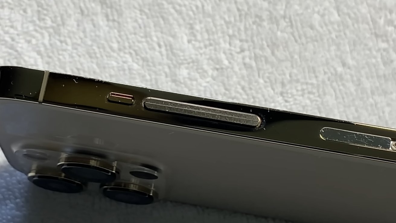 Close-up of a smartphone's side, showing camera lenses, buttons, and frame against a textured surface.