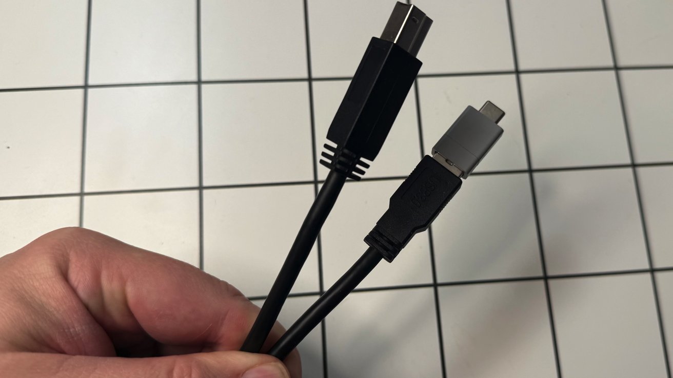 A hand holds two cables with USB and connectors against a tiled background.