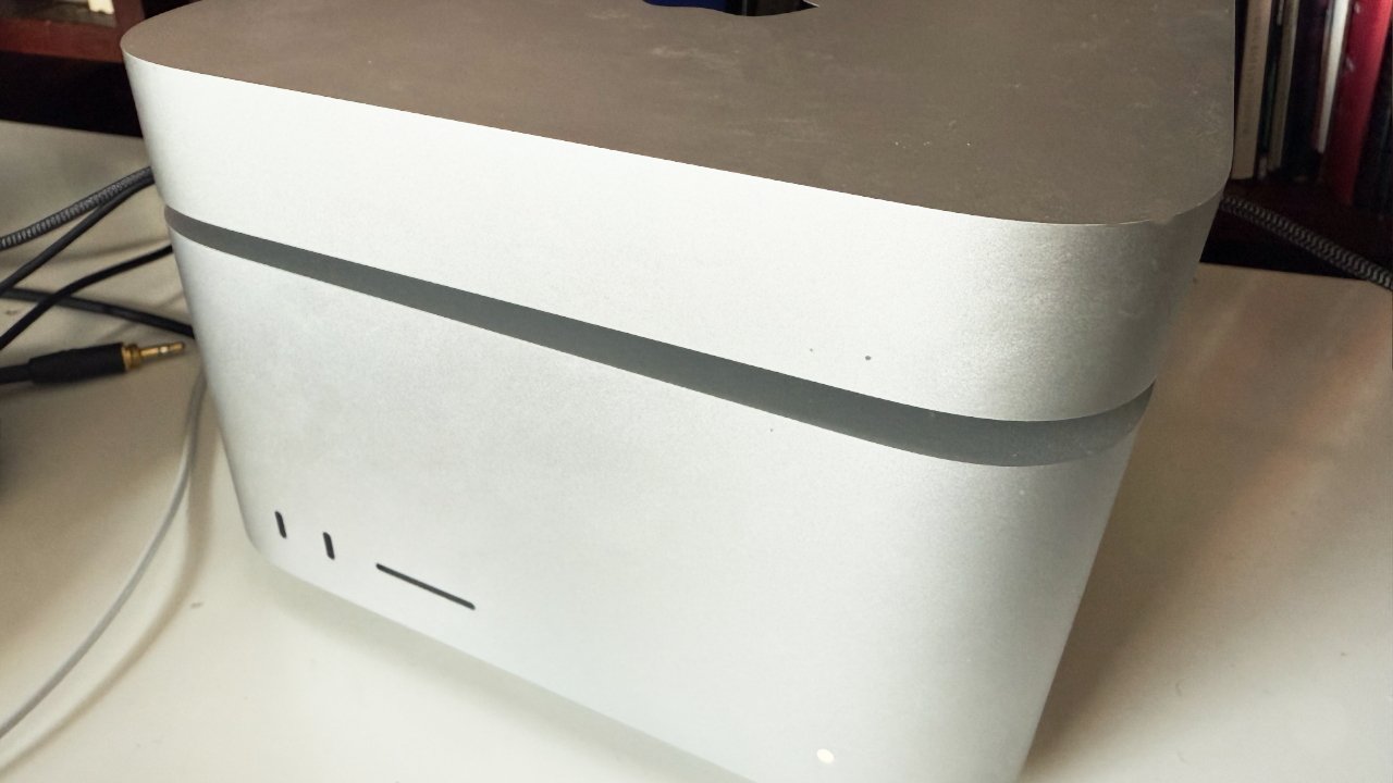 A sleek, curved silver desktop computer with minimal design, showing a few indistinct ports on its side and cords extending from the back.