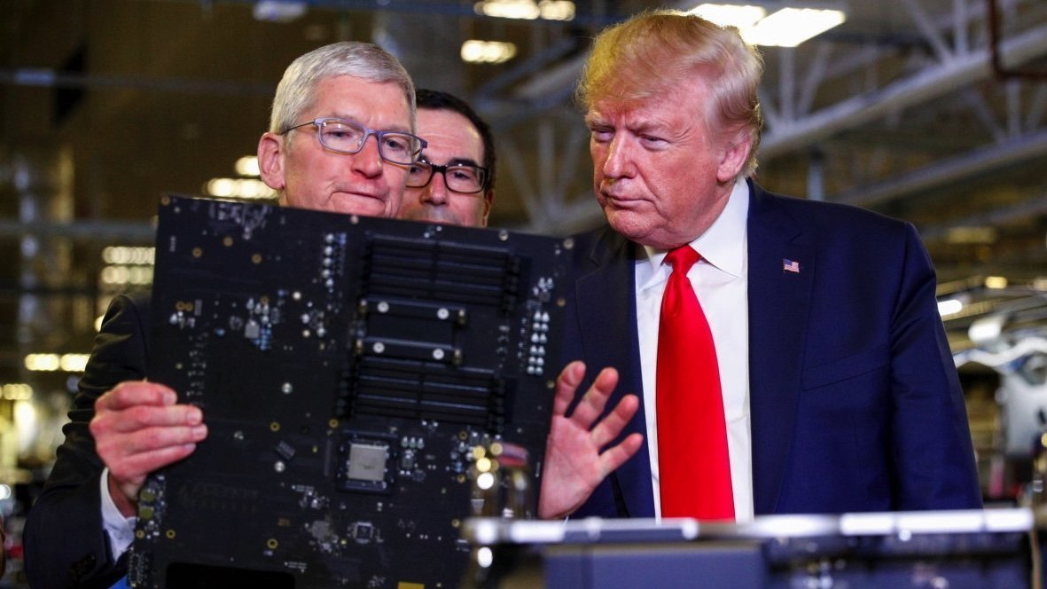 Three men in suits examine a large circuit board in a brightly lit industrial setting.