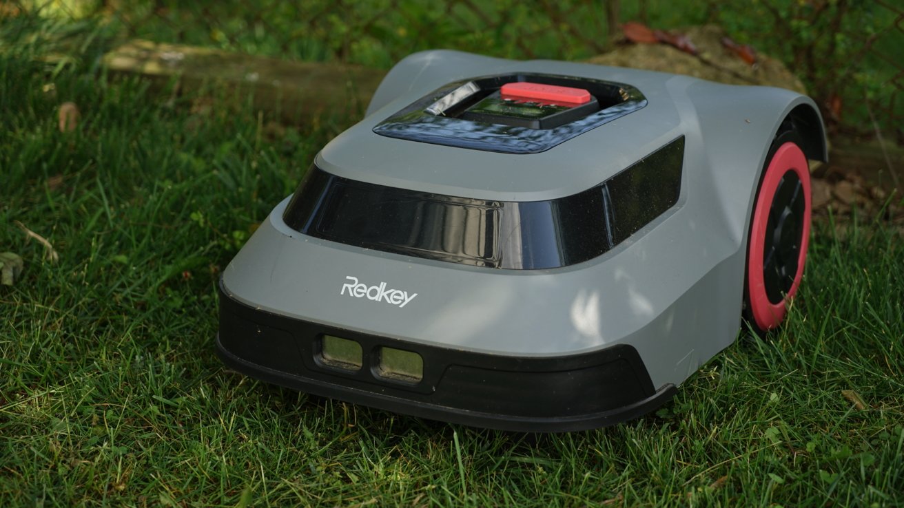 A gray robotic lawn mower with red wheels and a black trim, labeled 'Redkey,' on green grass.