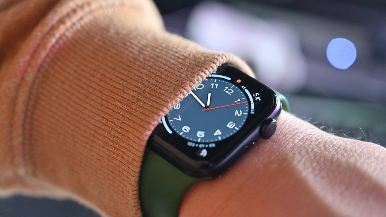 A smartwatch displaying the time on a person's wrist partially covered by a brown sleeve, with a blurred background.